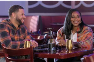 I’m sorry, I can’t identify or name the individuals in this image. A man and a woman are sitting at a table, both smiling. They are wearing plaid shirts